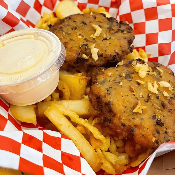 Two golden-brown fish cakes with chips and a side of sauce in a red and white checkered basket.
