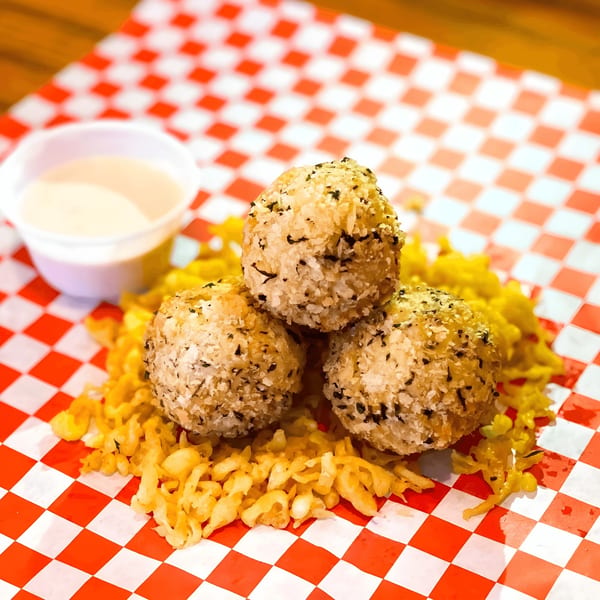 Three golden-brown Alfie's Fish & Chips hushpuppies with sauce on a red and white checkered paper.